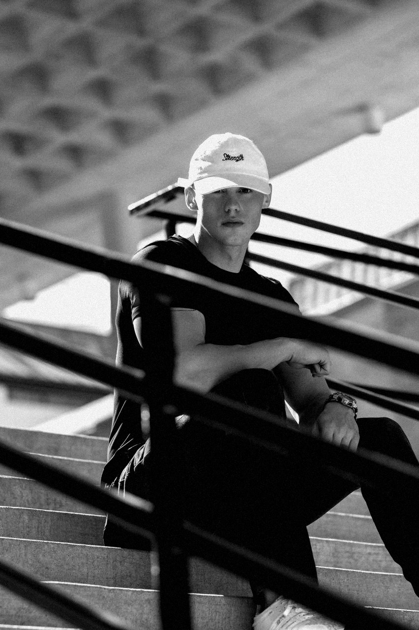 Seated on concrete steps in the Strength cap and Signature Tee